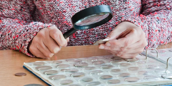 Collector examining coins with magnifying glass for grading – coin grading guide