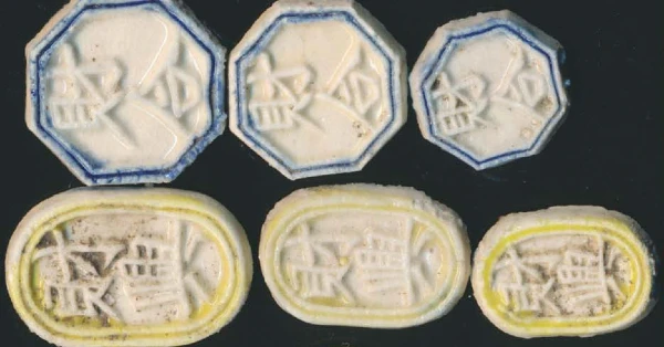 Collection of antique Siamese gambling tokens in octagonal and oval shapes with Chinese characters, showing blue and yellow glazed porcelain varieties